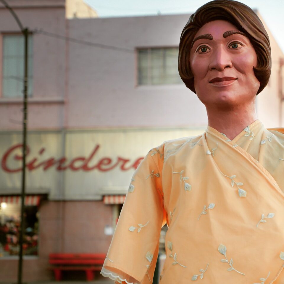 Large female puppet standing in front of a store named Cinderella